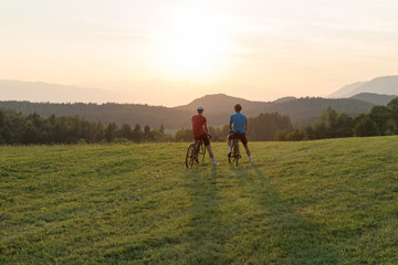 Professional cyclist couple taking a break on a green meadow and watching amazing mountain sunset, aerial shot. © 24K-Production