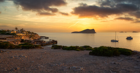 Beautiful sunset on the cliffs of Cala Comte, on the Island of Ibiza, Balearic Islands, Spain, where you can see pleasure boats, typical Ibizan houses and islets in the Mediterranean Sea