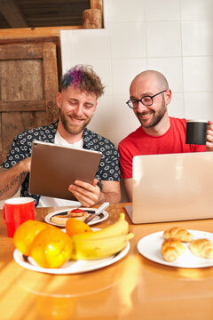Couple of gay men in the kitchen having breakfast with the laptop