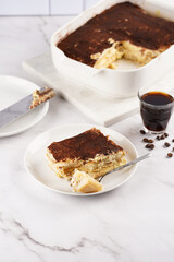 A piece of italian dessert tiramisu made of ladyfinger biscuits, mascarpone cheese, espresso on white marble background
