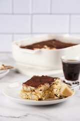 A piece of italian dessert tiramisu made of ladyfinger biscuits, mascarpone cheese, espresso on white marble background