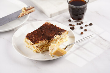 A piece of italian dessert tiramisu made of ladyfinger biscuits, mascarpone cheese, espresso on white marble background