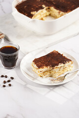A piece of italian dessert tiramisu made of ladyfinger biscuits, mascarpone cheese, espresso on white marble background
