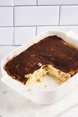 A piece of italian dessert tiramisu made of ladyfinger biscuits, mascarpone cheese, espresso on white marble background