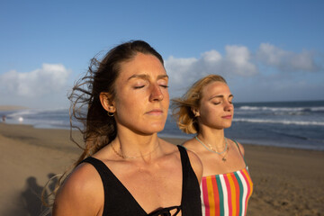 portrait of young women meditating with their eyes closed on the beach