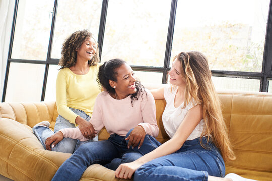 Three young multiracial girls talking sitting at sofa living room home.