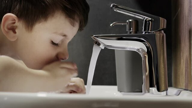 A little preschooler turns on the faucet and washes his face in the bathroom.