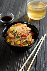 Asian rice noodles funchose with chicken, vegetables and sauce. Near chopsticks and green tea