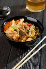 Asian rice noodles funchose with chicken, vegetables and sauce. Near chopsticks and green tea