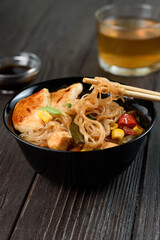 Asian rice noodles funchose with chicken, vegetables and sauce. Near chopsticks and green tea