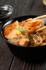Asian rice noodles funchose with chicken, vegetables and sauce. Near chopsticks and green tea