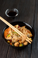 Asian rice noodles funchose with chicken, vegetables and sauce. Near chopsticks and green tea