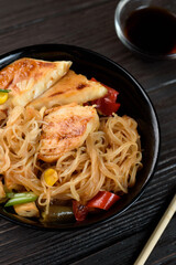 Asian rice noodles funchose with chicken, vegetables and sauce. Near chopsticks and green tea