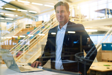 Whatever you do, do it well. Portrait of a well-dressed businessman using his laptop while standing in the office.