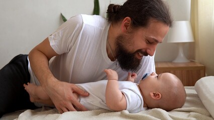 Authentic Young Bearded Man Holding Newborn Baby. Dad And Child Son On Bed. Close-up Portrait of Smiling Family With Infant On Hands. Happy Marriage Couple On Background. Childhood, Parenthood Concept