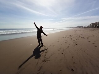 hombre  con sombrero, brazos abiertos y su sombra en la playa