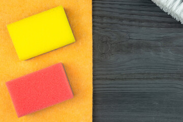 Sponges, brush and washcloth for washing dishes on a dark wooden table (copy space).