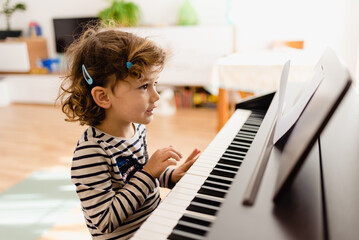Adorable little girl sitting at the piano experimenting with musical notes while smiling.