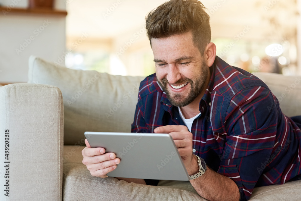 Poster Playing catch up with life online. Shot of a relaxed young man using a digital tablet on the sofa at home.