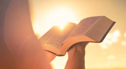Person holding reading bible up to the sunlight - obrazy, fototapety, plakaty