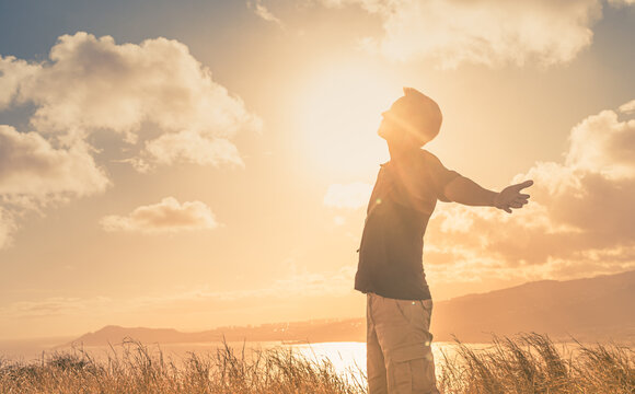 It's a beautiful life! Young man with arms up to the sunlight standing in a meadow field.