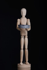 Human wooden figure holds in hands a dental upper jaw model printed on 3d printer on a black background.