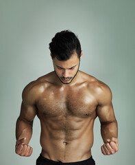 Fototapeta premium Feeling pumped. Studio shot of an athletic young man flexing his muscles against a gray background.