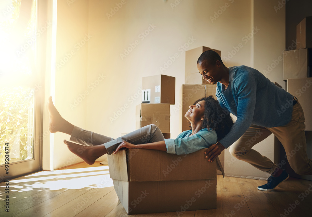 Poster go faster. shot of a cheerful young man pushing his girlfriend around in a cardboard box at home dur