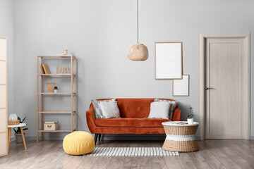 Interior of modern room with comfortable sofa, pouf and blank photo frames on light wall