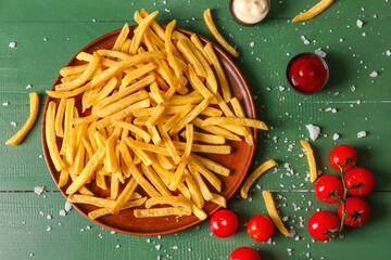 Plate with tasty french fries and tomatoes on green wooden background