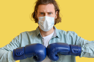 Young man wearing medical mask and boxing gloves on color background. Concept of strong immunity