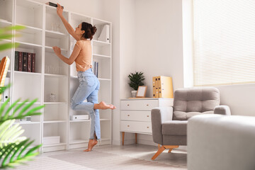 Young barefoot woman taking book from shelf at home