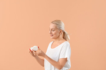 Mature blonde woman with jar of cream on beige background