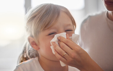 Weve been doing this all day. Shot of a mother wiping her little girls nose with a tissue in bed at...