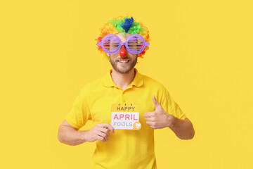Funny young man in disguise and with card on yellow background. April fools' day celebration