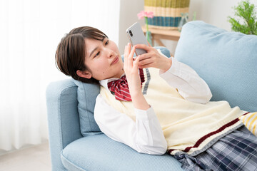 ソファーでスマートフォンを操作する女子高生
