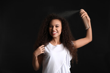 Pretty young African-American woman with hair spray on black background