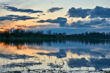 Obraz na płótnie Canvas Spring landscape with dramatic after-sunset sky reflected in the water, silhouettes of trees on the shore. Evening calm on the river. Bright afterglow.
