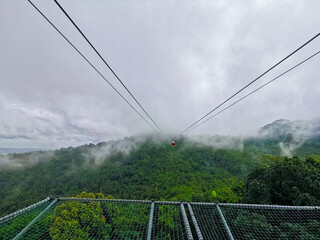 Bright red cable car with double safety sling to the cloudy misty forest in highland mountain in...