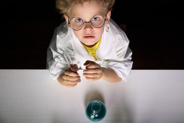 Serious little boy in white uniform and glasses conducts chemical experiments in laboratory. Young...