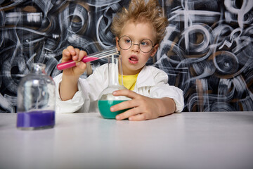 Beautiful little boy scientist is intrigued and excited, exploring colored chemical liquids in the...
