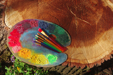 Artist palette, artistic brushes on a tree stump in a spring forest.