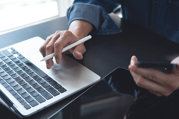 Close up of business man working on laptop computer and using mobile phone, surfing the internet with digital tablet on office table