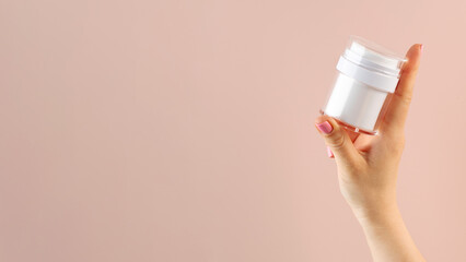 A mock-up of a jar of moisturizer in a woman's hand on a pink background. Copy space. 