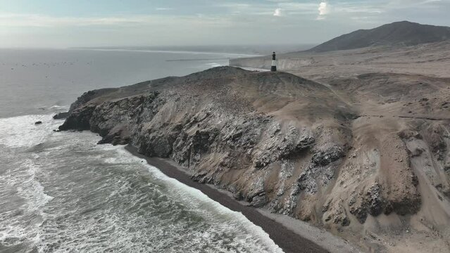 Aerial view of the waves breaking on the cliffs with sea birds and a lighthouse.Half Moon beach, Puerto Eten, Lambayeque, Peru.