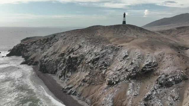Aerial view of the waves breaking on the cliffs with sea birds and a lighthouse.Half Moon beach, Puerto Eten, Lambayeque, Peru.