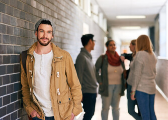 Cool guy on campus. Portrait of a young male university student standing in a campus corridor with his classmates in the background.