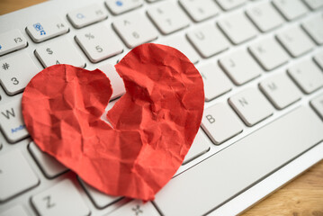 Red broken heart paper on white keyboard computer background. Online internet romance scam or swindler in website application dating concept. Love is bait or victim. - obrazy, fototapety, plakaty