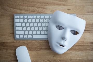Flat lay white scary half face mask, keyboard and mouse on wooden table background in dark tone. Hacker, cybercrime, romance scam and online security concept.