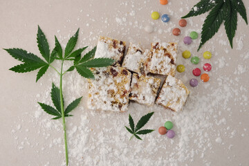 Craft sweets with cannabis on ivory background. Layout with marijuana leaves, candy confetti and powdered sugar, top view, flat lay.